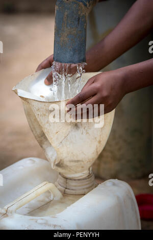 Kleine Hände halten einen Trichter, so dass ein wasserkrug von einer Pumpe in Ganta gefüllt werden kann, Liberia Stockfoto