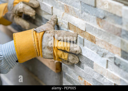 Nahaufnahme der Arbeiter in Schutz handschuhe Drücken der Fliese in der Zement an der Wand während Fliesen eine Wand mit verzierten Fliesen l in einem DIY, modern Stockfoto