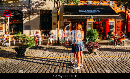 Sevilla, Spanien - 14 Juli, 2018: Paar erfasst einen selfie auf einer Straße mit Kopfsteinpflaster mit Restaurant Terrassen im historischen Zentrum von Sevilla. Stockfoto