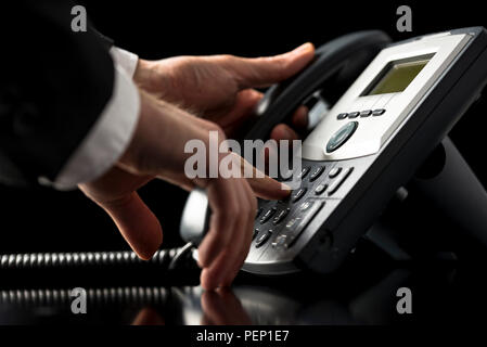 Niedrigen winkel Detailansicht der Hände von einem Geschäftsmann im Anzug, wählen auf einem Telefon mit einer DFÜ-desktop Festnetz Instrument, als er drücken Sie anrufen Stockfoto
