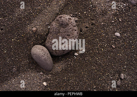 Schwarzer Sandstrand Hintergrund mit Vulkangestein Stockfoto