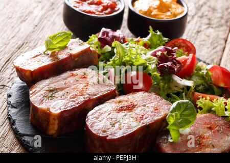 Gebratene Rippchen und frisches Gemüse Salat. Mit Ketchup und Senf auf einer Schiefertafel Teller serviert. Horizontale Stockfoto