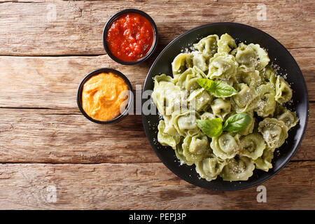 Gekochten Spinat grün Cappelletti, Ravioli, Tortellini, gefüllt mit Fleisch mit Parmesan und Basilikum serviert mit Saucen close-up auf dem Tisch. horiz. Stockfoto