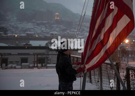 Am 24. Januar 2016, an Bord der USS Ashland (LSD 48) in Sasebo, Japan, senken die Seeleute das Fähnrich während der Abendfarben auf dem Cockpit ab. Das amphibische Dock-Landungsschiff, Teil der Bonhomme Richard Amphibious Ready Group, führt die geplante kontinuierliche Wartungsverfügbarkeit (CMAV) durch, um die ordnungsgemäße Wartung, die Betriebsbereitschaft und die Einhaltung der Zeremonienverfahren auf See an Bord des Schiffes bei schneereichen Bedingungen sicherzustellen. Stockfoto