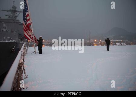 Am 24. Januar 2016, an Bord der USS Ashland (LSD 48) in Sasebo, Japan, senken die Seeleute das Fähnrich während der Abendfarben auf dem Cockpit ab. Das amphibische Dock-Landungsschiff, Teil der Bonhomme Richard Amphibious Ready Group, ist dabei, seine geplante kontinuierliche Wartungsverfügbarkeit (CMAV) abzuschließen, um die ordnungsgemäße Wartung, Betriebsbereitschaft und die Einhaltung der feierlichen Vorschriften an Bord des Schiffes zu gewährleisten. Stockfoto