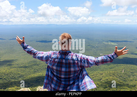 Man genießt die Aussicht von der Spitze des Berges. Ansicht der Rückseite des jungen Mann stand draußen mit ausgebreiteten Armen gegen lendscape. Stockfoto