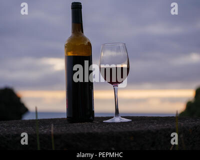 Wein Flasche und Glas mit dem Sonnenuntergang Himmel und Meer im Hintergrund. Nach oben Schließen Stockfoto
