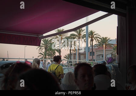 PALMA DE MALLORCA, SPANIEN - 23. JUNI 2018: Blick von der Terrasse bei Sonnenuntergang mit Palmen und Menschen aus dem Innenraum in einer Bar am 23. Juni 2018 in Palma de Mallorc Stockfoto