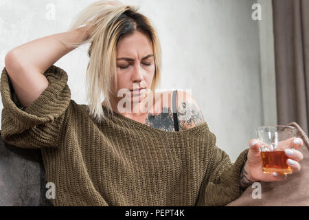 Porträt einer schönen Frau, die Kopfschmerzen hat, mit einem Glas Whiskey in der Hand. Stockfoto