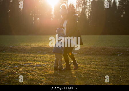 Schwangere Frau mit Kind im Feld spielen im Freien bei Sonnenuntergang, drücken Kid neben dem Magen. Stockfoto