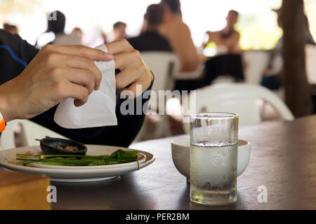 Hand mit weißen Seidenpapier nach Ende Mittagessen mit Glas Wasser auf dem Tisch. Stockfoto