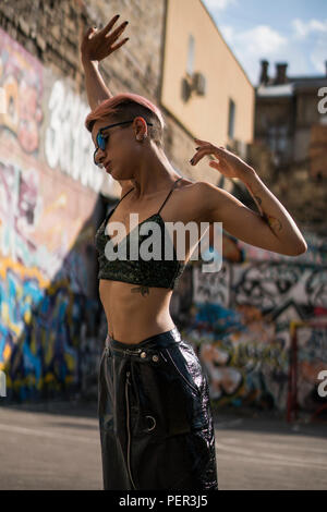 Street Punk oder Hippie Mädchen mit in Sonnenbrille rosa gefärbte Haare. Frau mit Piercing in der Nase, Ohren Tunnel und ungewöhnliche Frisur am Basketballplatz wit Stockfoto