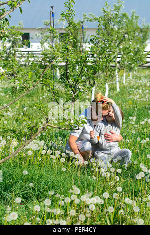 Ein kleines Mädchen und eine erwachsene Frau junge Bäume gepflanzt. Junge Bäume Blüte weiße Blumen vor dem Hintergrund des grünen Grases und gelben Löwenzahn. Rep. Stockfoto