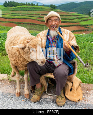 Ein alter chinesischer Mann verkleidet mit der traditionellen Kleidung, während die Landschaft von DongChuan in der Provinz Yunnan, China genießen. Stockfoto