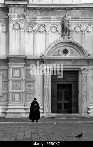 Einsamer Mann in einem schwarzen Cape steht außerhalb der Chiesa di San Zaccaria, Castello, Venice, Italien. Schwarz und Weiss Stockfoto