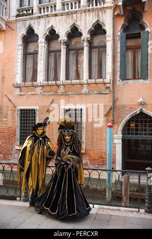 Zwei carnevale Nachtschwärmer in wunderschönen Schwarz und Gold Kostüme Pose vor dem Palazzo Priuli und der Rio di San Provolo, Castello, Venice, Italien Stockfoto