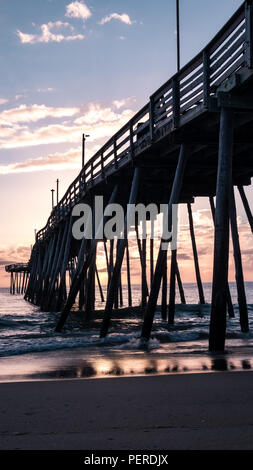 Wunderschöne rot und pink sunrise in das Wasser unter einem hölzernen Fishing Pier wider. Stockfoto