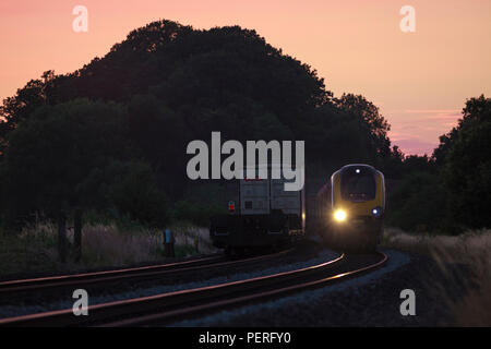 Länderübergreifende Züge Voyager Passagier Zug passiert ein Freightliner intermodalen Container Freight Train Funkeln in den Sonnenuntergang im Cherwell Valley UK Stockfoto