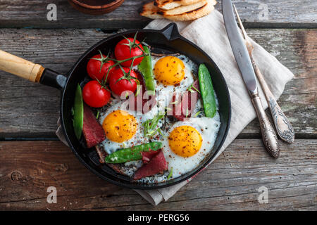 Spiegelei in der Pfanne mit Cherry Tomaten, grüne Erbsen und Pastrami. Copyspace Stockfoto