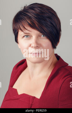 Closeup Portrait von schönen Lächeln im mittleren Alter weiße Kaukasier brünette Frau mit blauen Augen im roten Kleid, in Kamera suchen, auf hellen Hintergrund ich Stockfoto
