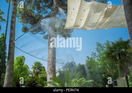 Markise und Sprinkler spritzt verdampft Wasser bei öffentlichen Park. Geräte für die Kühlung der heißen Sommer Temperatur in Spanien im Freien Stockfoto