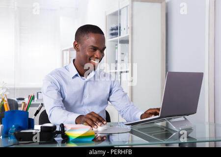 Portrait der junge lächelnde Geschäftsmann mit Laptop am Arbeitsplatz Stockfoto