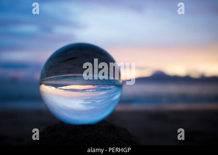 Rosa Blau und Grau Sonnenuntergang über dem Ozean mit Wolken durch Glas Kugel genommen Stockfoto