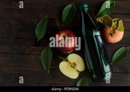 Eine Flasche Apfelessig mit frischen Äpfeln und grüne Blätter auf hölzernen Hintergrund. Copyspace links. Stockfoto