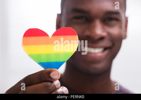 Lächelnder Mann mit Rainbow Herz in seine Hand gegen den weißen Hintergrund Stockfoto