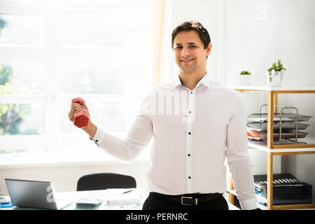 Junge Unternehmer Trainieren mit einem roten Hantel in Office Stockfoto