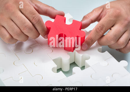 Nahaufnahme der Hand ein Geschäftsmann Anschluss rot Stück in Weiß Jigsaw Puzzles Stockfoto