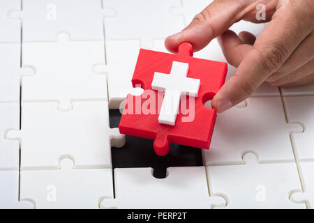 Nahaufnahme einer Hand, rote Kreuz symbol Stück in Puzzle Stockfoto