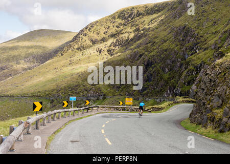 Ein Radfahrer steigt die schmale, kurvenreiche und steile Conor Pass Straße durch die Berge der Halbinsel Dingle in der Grafschaft Kerry in Irland. Stockfoto