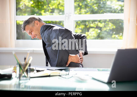 Seitenansicht eines reifen Unternehmer leiden unter Rückenschmerzen im Büro Stockfoto