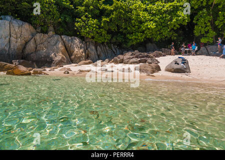 Nach einem Schnorchelausflug, Touristen sind das Essen an den felsigen Teil der Rawa Strand unter den Schatten der Bäume, während die Fische schwimmen im flachen... Stockfoto