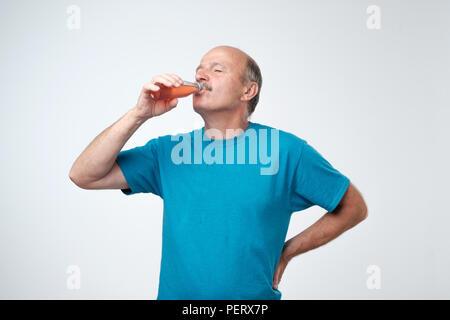 Portrait von attraktiven kaukasischen Mann im blauen T-Shirt stehen und trinken Limo über grauer Hintergrund Stockfoto