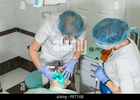 Frau beim Zahnarzt Klinik erhält der zahnmedizinischen Behandlung ein Loch in einen Zahn zu füllen. Zahnersatz und Verbundmaterial Polymerisation mit UV-Licht und Laser. Stockfoto