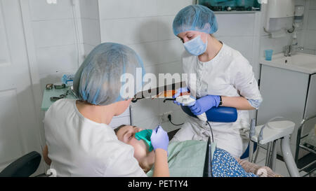 Frau beim Zahnarzt Klinik erhält der zahnmedizinischen Behandlung ein Loch in einen Zahn zu füllen. Zahnersatz und Verbundmaterial Polymerisation mit UV-Licht und Laser. Stockfoto