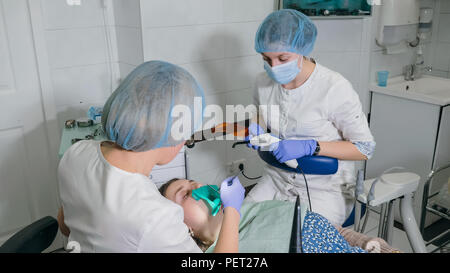 Frau beim Zahnarzt Klinik erhält der zahnmedizinischen Behandlung ein Loch in einen Zahn zu füllen. Zahnersatz und Verbundmaterial Polymerisation mit UV-Licht und Laser. Stockfoto