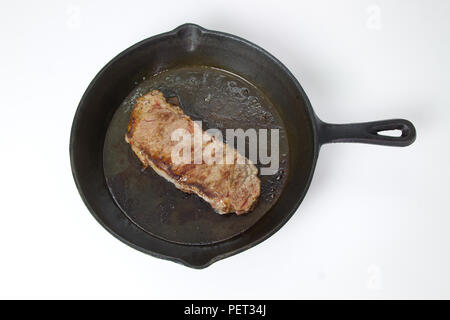 Beef Steak braten in einer gusseisernen Pfanne auf weißem Hintergrund mit Raum für Text isoliert Stockfoto