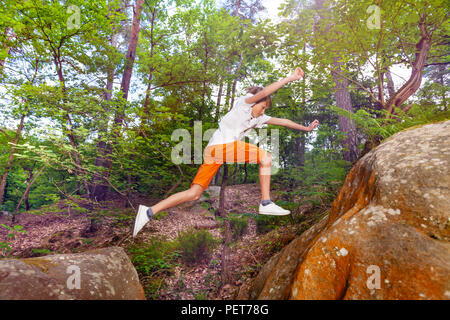 Porträt eines Jungen lange Sprung von einem Felsen im Wald zu Staubbeutel Stockfoto