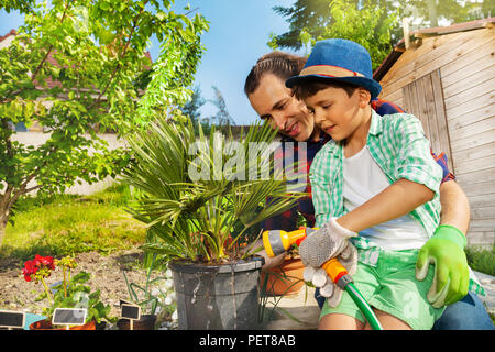 Gerne Vater Lehre sein kleiner Sohn Wasser Pflanzen mit Hilfe der Sprinkleranlage im Garten Stockfoto