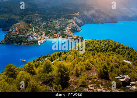 Atemberaubende Sicht von oben nach Assos Dorf mit lokalen Häusern. Platz Sehenswürdigkeit von Kefalonia. Einsame weiße Yacht an in ruhigen wunderschönen Lagune, umgeben von Pinien und Zypressen umgeben verankern. Griechenland Stockfoto