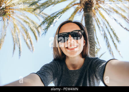 Junge schöne Frau touristische oder Blogger macht einen selfie oder Berichterstattung an seine Abonnenten auf dem Hintergrund der Palmen in einem heißen Land. Stockfoto