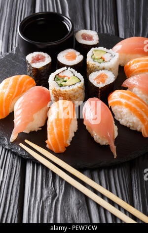 Ein japanisches Menü. Lecker eingestellt von Sushi mit Lachs und Thunfisch, California Rolls, Maki, Sojasauce closeup auf einem schwarzen Schiefer Board auf dem Tisch. Vertikale Stockfoto