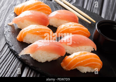 Schmackhafte Ernährung Sushi mit Lachs und Thunfisch, Sojasoße close-up auf einem schwarzen Schiefer auf einem Tisch. Horizontale Stockfoto