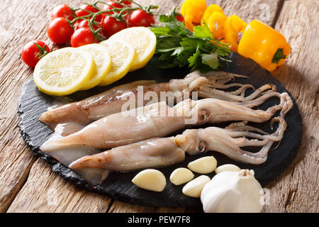 Essen Hintergrund: Rohe frische Kalmare close-up und Gemüse auf einem Schiefer Board auf einem Tisch. Horizontale Stockfoto