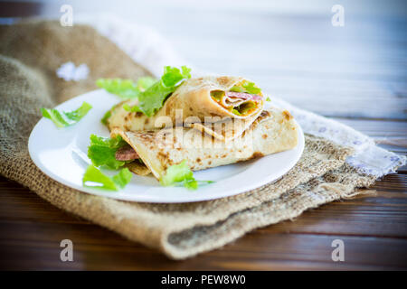 Dünne Pfannkuchen mit Salat und Speck in eine Platte auf einem Holztisch Stockfoto