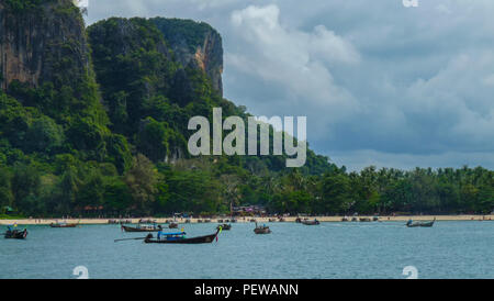 Landschaft auf einem der Strände der Provinz Krabi in Thailand, mit Dutzenden von Long-tail Boote auf dem Wasser, und Kalkfelsen an der Rückseite Stockfoto