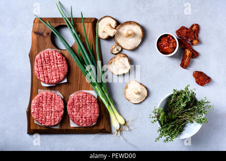 Rohe frische marmoriert Hackfleisch Steak und Würzmittel auf grauem Beton Hintergrund, Flach, Ansicht von oben Stockfoto